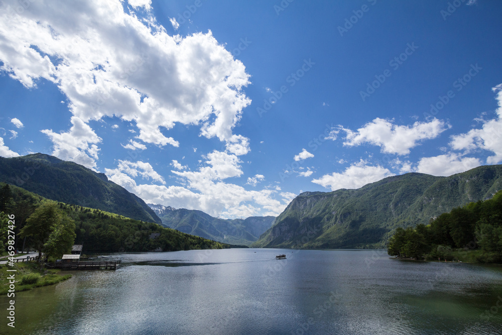 Panorama of Lake Bohinj, also called bohinjsko jezero, on a sunny afternoon, with a boat crusing on the waters. Bohinj lake is a major landmark of the Julian Alps mountain chain in Slovenia, Europe.