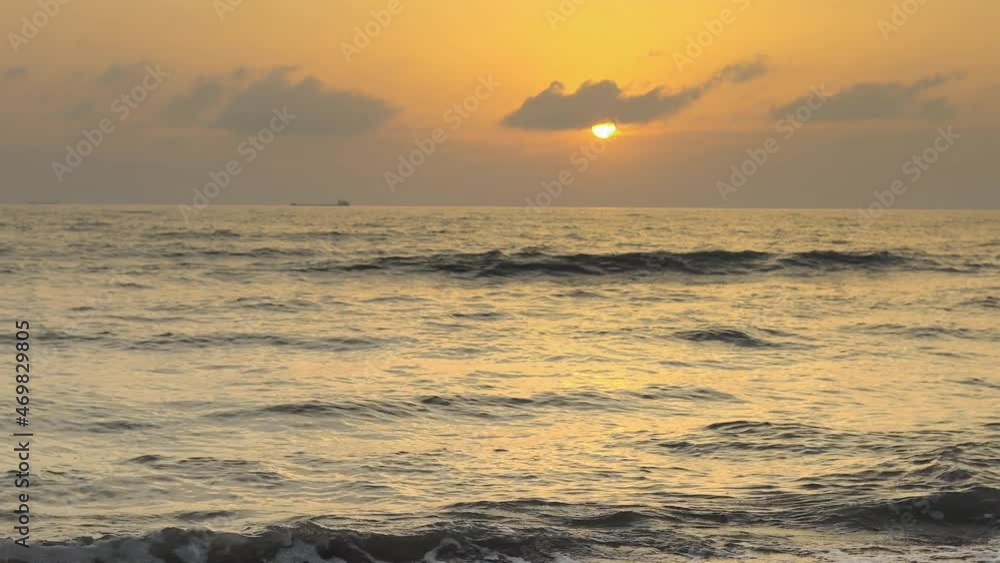 Waves crashing on the sandy sea, ocean shore with the sunset, sunrise rays reflecting. Sea waves breaking into splashes and white foam. Vacation and summer travel Waves crashing on the sandy sea, ocean shore with the sunset, sunrise rays reflecting. Sea waves breaking into splashes and white foam. Vacation and summer travel