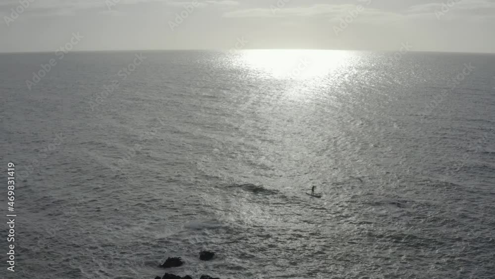 Grey ocean aerial ascends, retreats from SUP paddleboarder near rocks Grey ocean aerial ascends, retreats from SUP paddleboarder near rocks