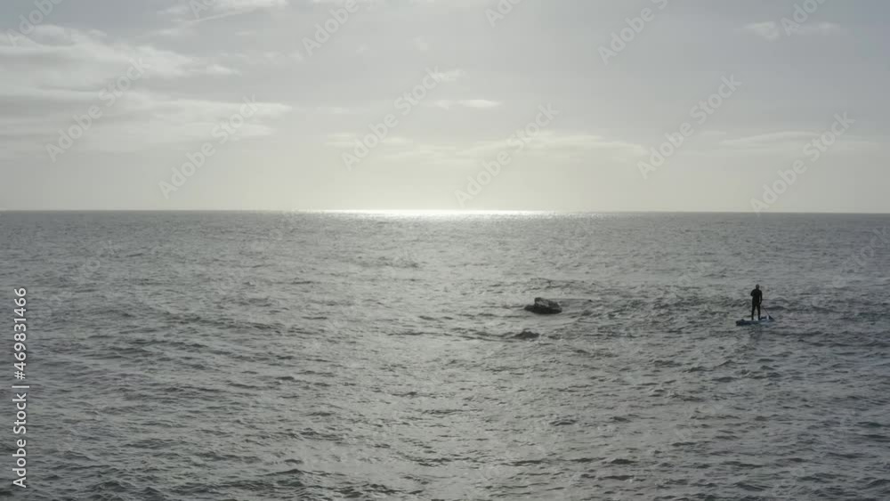 Stand up paddleboarder pulls past rock boomer toward ocean horizon Stand up paddleboarder pulls past rock boomer toward ocean horizon