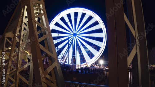 Timelapse of ferris wheel in Cologne near Schokoladenmuseum (Choclate museum). Spinning and stopping with long exposure. Old Bridge in goreground. Blue lights and a smooth camera movment and zoom. V1 photo