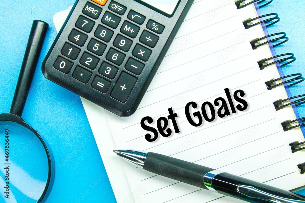 magnifying glass, calculator, pen and notes with the word set goals magnifying glass, calculator, pen and notes with the word set goals