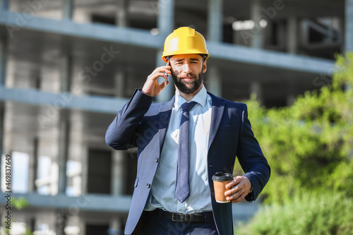 Industrial engineer with cup of coffee talking by mobile phone outdoors