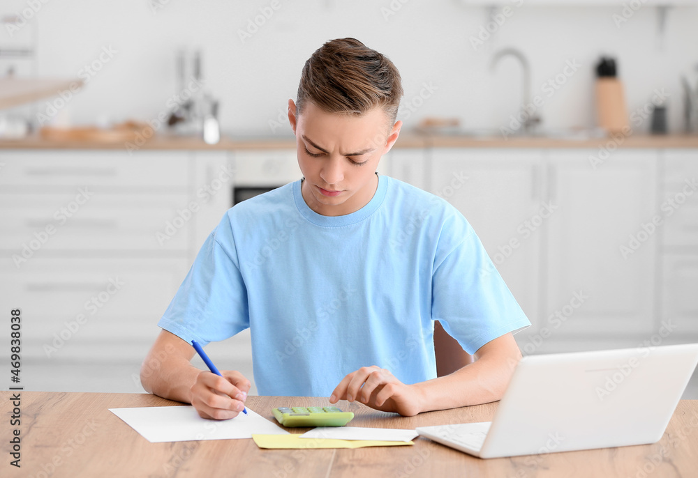 Teenage boy using calculator at table in kitchen Teenage boy using calculator at table in kitchen