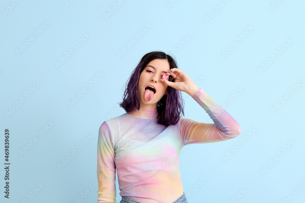 Stylish young woman with pink chewing gum showing tongue on blue background Stylish young woman with pink chewing gum showing tongue on blue background