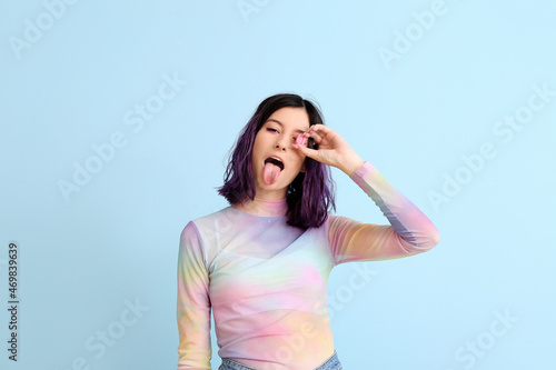 Stylish young woman with pink chewing gum showing tongue on blue background