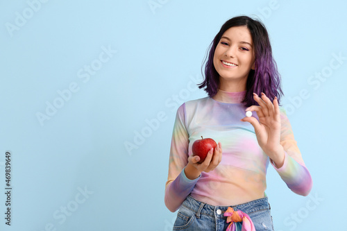 Stylish young woman with chewing gum and apple on blue background