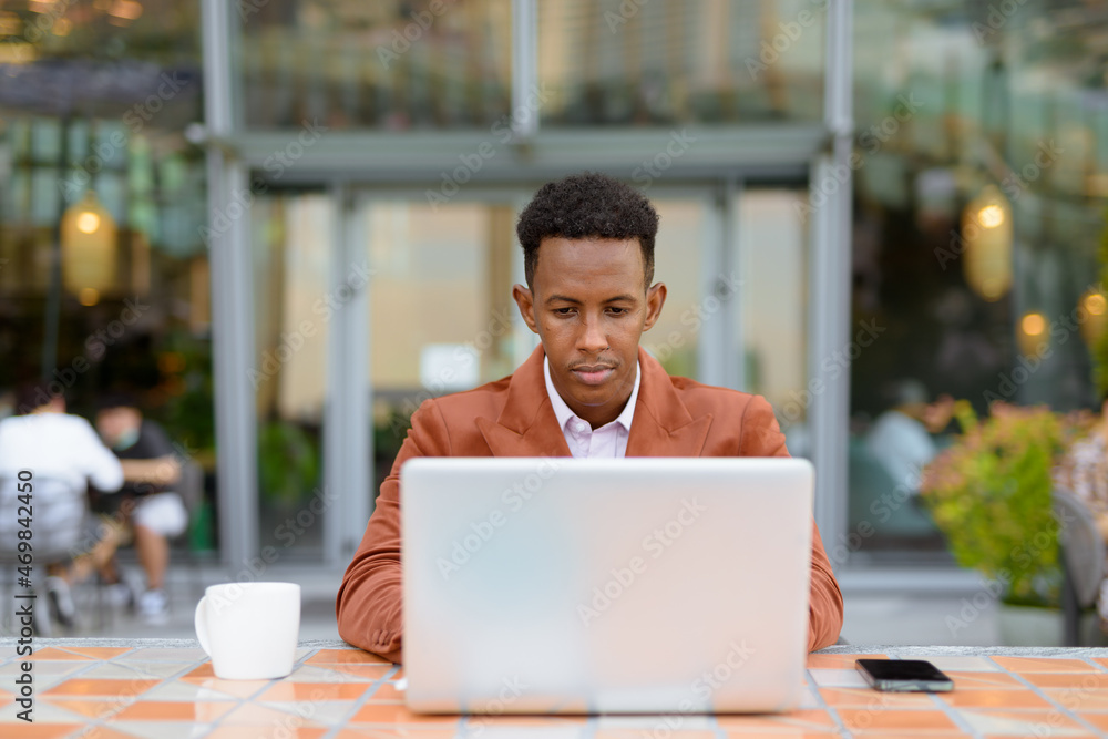African businessman outdoors in coffee shop using laptop computer African businessman outdoors in coffee shop using laptop computer
