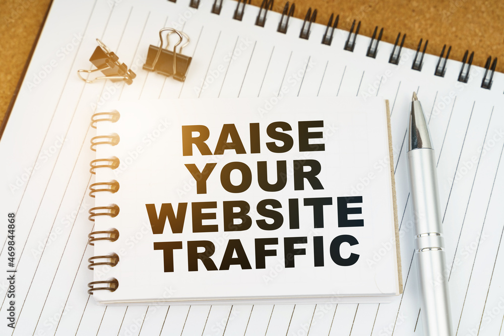 On the table there is a pen, clamps and a notebook with the inscription - RAISE YOUR WEBSITE TRAFFIC On the table there is a pen, clamps and a notebook with the inscription - RAISE YOUR WEBSITE TRAFFIC