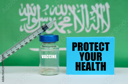 Vaccine, syringe and blue plate with the inscription - PROTECT YOUR HEALTH. In the background the flag of Saudi Arabia