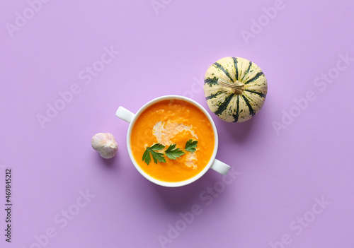 Pot with delicious pumpkin cream soup on purple background