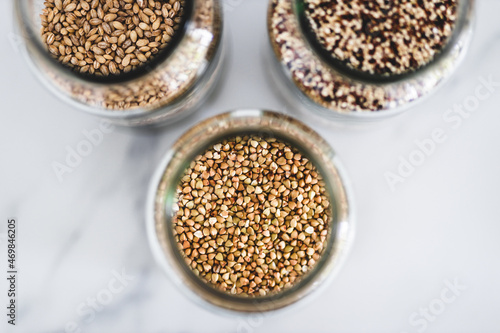 healthy whole grains and legumes in clear pantry jars on marble background including quinoa buckwheat and barley,, simple ingredients concept