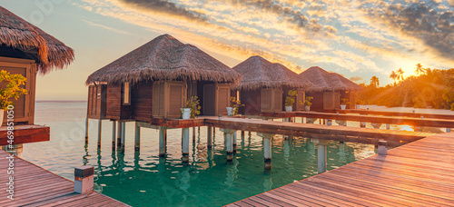 Sunset on Maldives island, luxury water villas resort hotel and wooden pier. Colorful sky and clouds and beach background for summer vacation holiday, traveling destination. Paradise sunset landscape