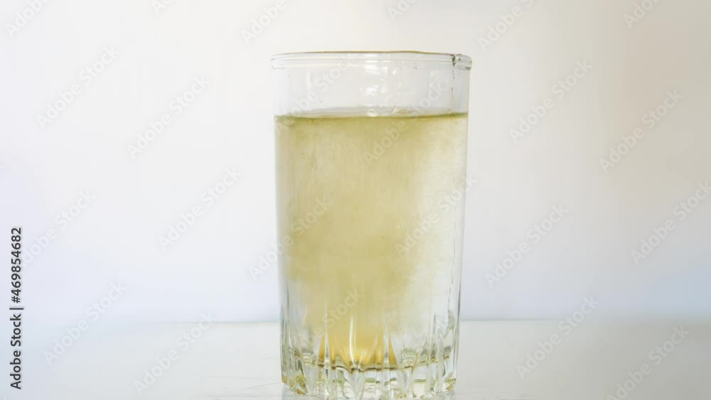 Close-up of a dissolving pill in a glass of water against white background Close-up of a dissolving pill in a glass of water against white background
