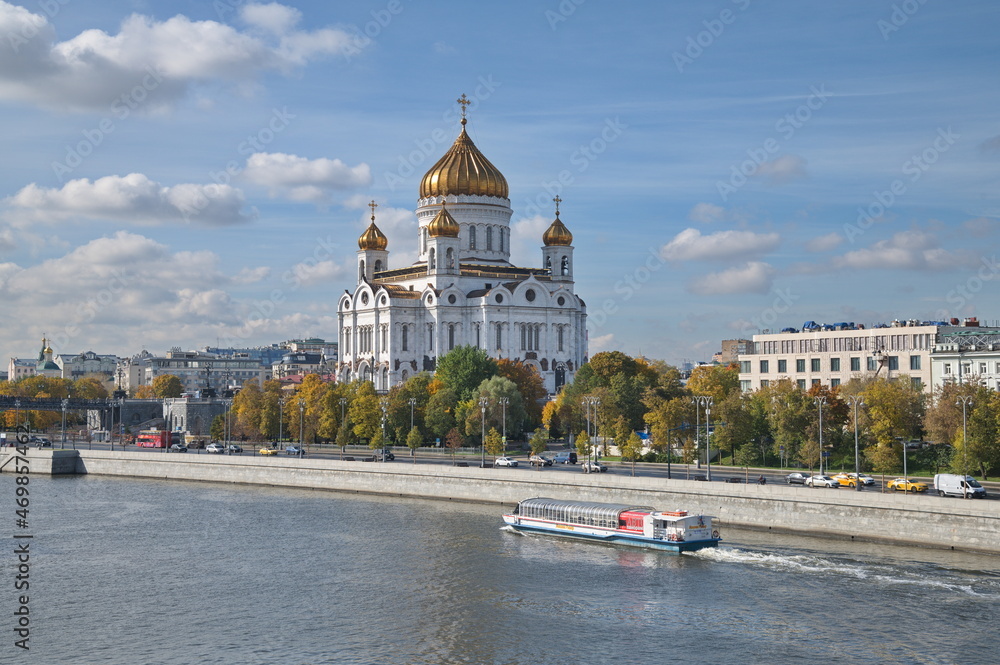 Obraz premium Moscow, Russia - September 29, 2021: Autumn view of the Cathedral of Christ the Savior, the Prechistenskaya embankment and a pleasure boat sailing along the Moscow-River