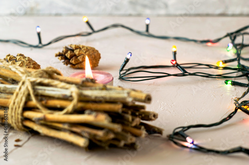 a burning candle pine cones a bundle of brushwood and a Christmas tree garland on a roughly plastered surface