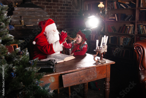 a little girl in an elf costume for the New Year and Christmas sits at a huge table elf and Santa Klaus