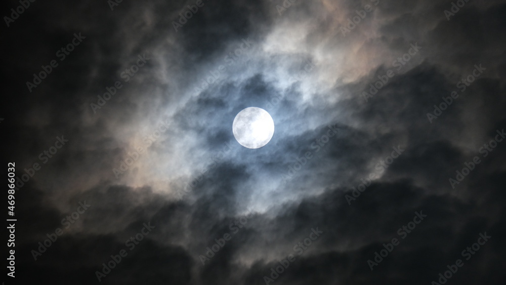 The beautiful full moon is shining with the white clouds in the sky at night in Bangkok, Thailand.