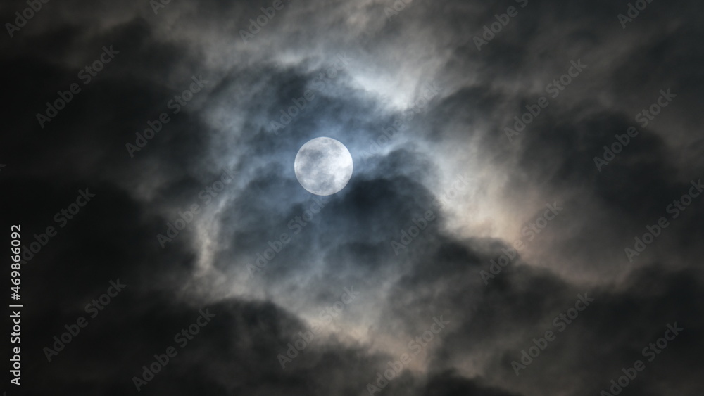 The beautiful full moon is shining with the white clouds in the sky at night in Bangkok, Thailand.