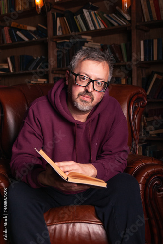 A man on the background of a bookcase with space for text or advertising. Brutal man with glasses 50 years old
