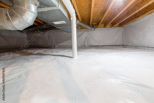 Crawl space fully encapsulated with thermoregulatory blankets and dimple board. Radon mitigation system pipes visible. Basement location for energy saving home improvement concept. photo