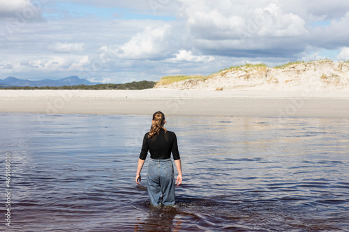 A teenage girl wading through a water channel on a wide sandy beach. photo