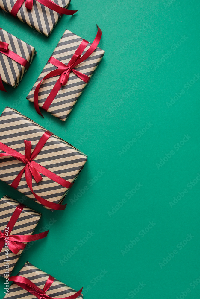 Fototapeta premium Striped craft gift box with black ribbon on a green. Valentines, Christmas or New Year day backdrop. Flat lay style with minimalistic design.