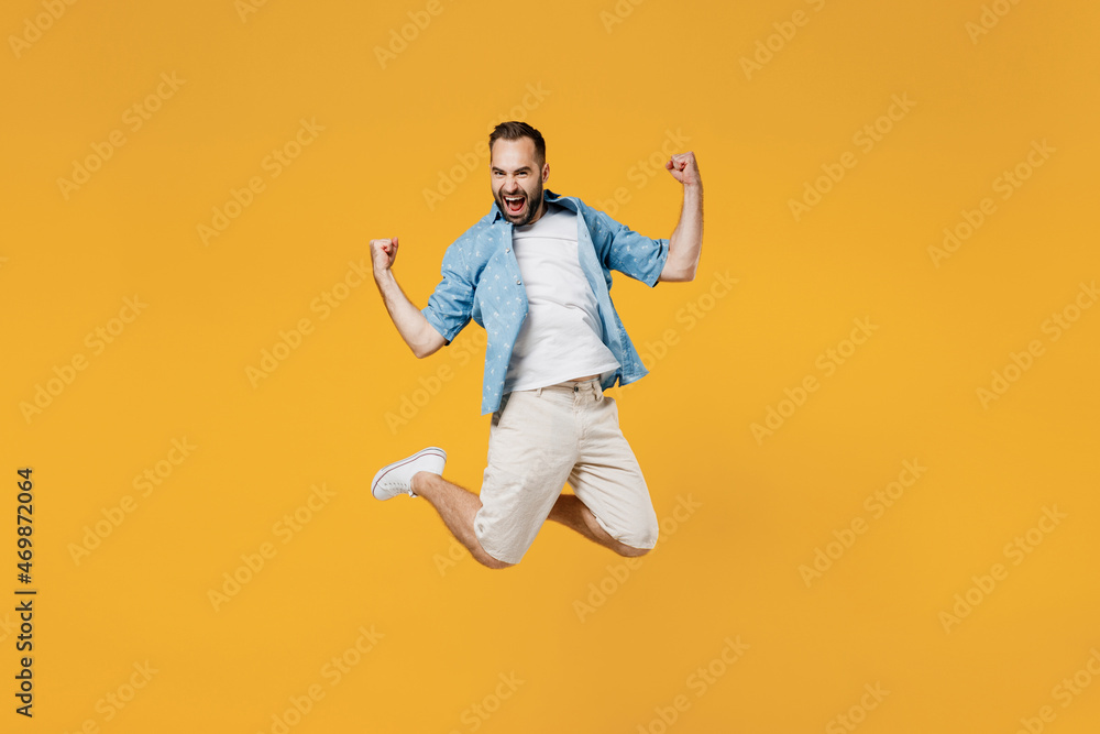 Full body young overjoyed satisfied happy caucasian man 20s wearing blue shirt do winner gesture clench fist jump high isolated on plain yellow background studio portrait. People lifestyle concept Full body young overjoyed satisfied happy caucasian man 20s wearing blue shirt do winner gesture clench fist jump high isolated on plain yellow background studio portrait. People lifestyle concept