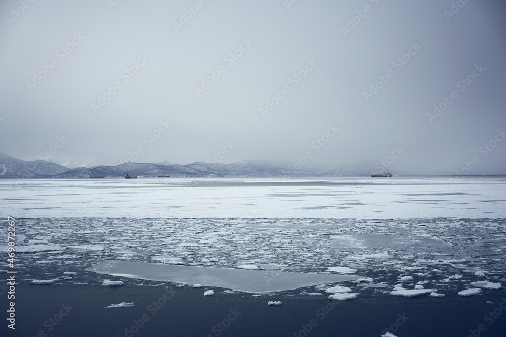 Winter landscape of the Avacha bay. Snowy mountains and ocean with ice floes at snowy weather. Kamchatka peninsula, Russia