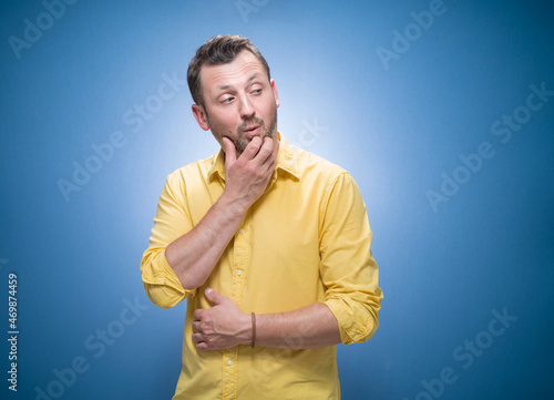 Distracted young man looking at other man over blue background, dresses in yellow shirt. Seducer man