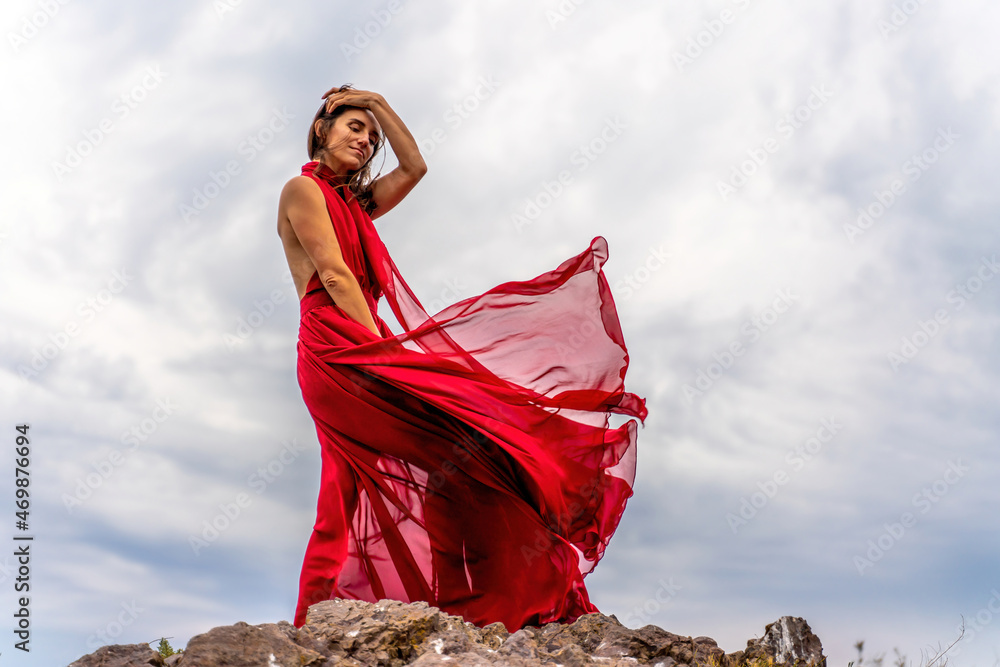 A woman in a red dress stands above a stormy sky, her dress fluttering, the fabric flying in the wind. A woman in a red dress stands above a stormy sky, her dress fluttering, the fabric flying in the wind.