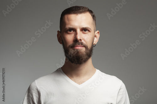 Male beauty concept. Emotive portrait of proud charismatic slim young bearded man posing over light gray background. Perfect haircut. Hipster style. Close up. Studio shot © Augustino
