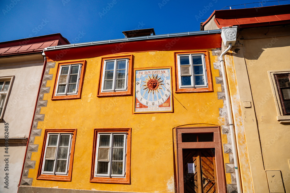 Kolin, Central Bohemia, Czech Republic, 10 July 2021: Narrow picturesque street with colorful renaissance baroque historical houses in medieval town center, sundial with the image of the sun