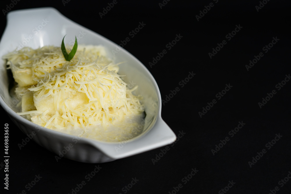 Singkong Thailand or called Thai sweet cassava serve with coconut milk and sprinkled with grated cheese on black background Singkong Thailand or called Thai sweet cassava serve with coconut milk and sprinkled with grated cheese on black background
