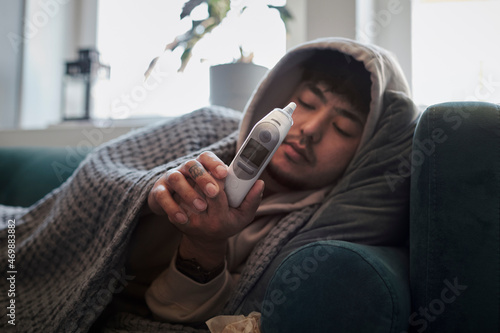 Ill man on sofa checking thermometer photo