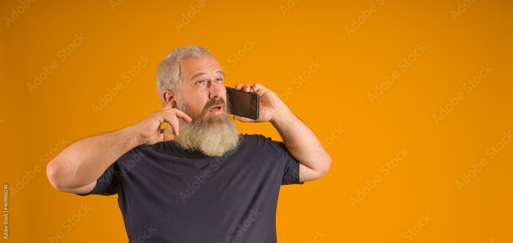 deaf man with gray beard and hair in a black t-shirt talking on the phone, yellow background deaf man with gray beard and hair in a black t-shirt talking on the phone, yellow background