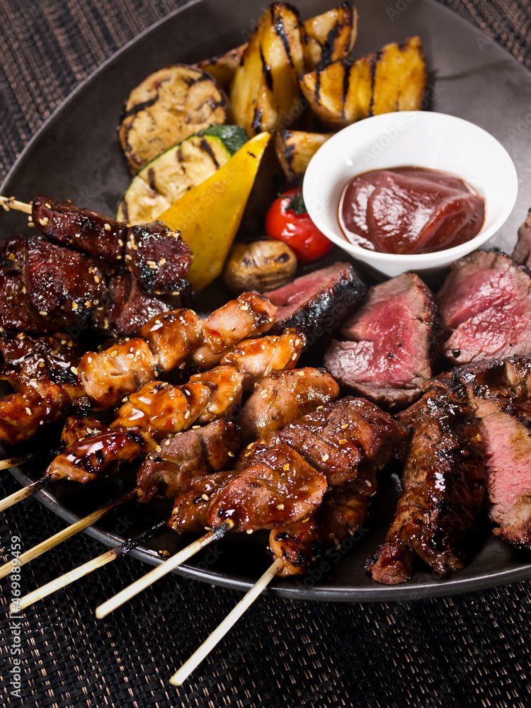 meat plate, set of different grilled skewers and grilled sliced filet mignon on a plate served with grilled vegetables, close up photo on a dark background