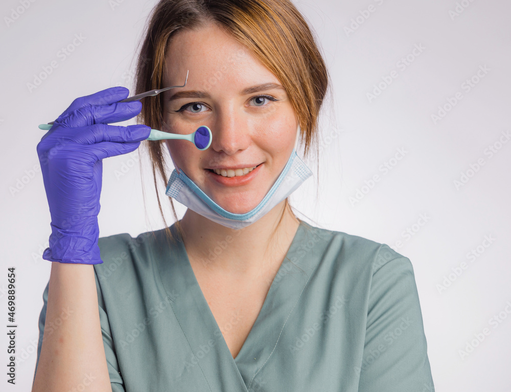Portrait of attractive smile female dentist with work tools, wearing uniform medical face mask and latex medical gloves on gray background Portrait of attractive smile female dentist with work tools, wearing uniform medical face mask and latex medical gloves on gray background