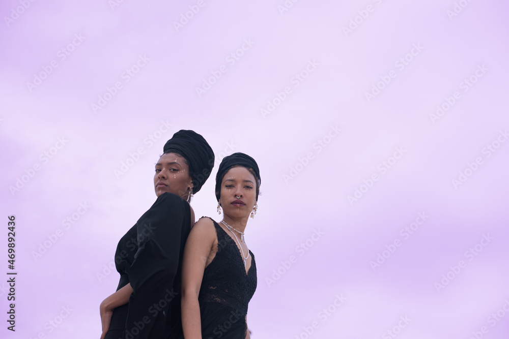 Low angle portrait of two ladies standing back to back Low angle portrait of two ladies standing back to back