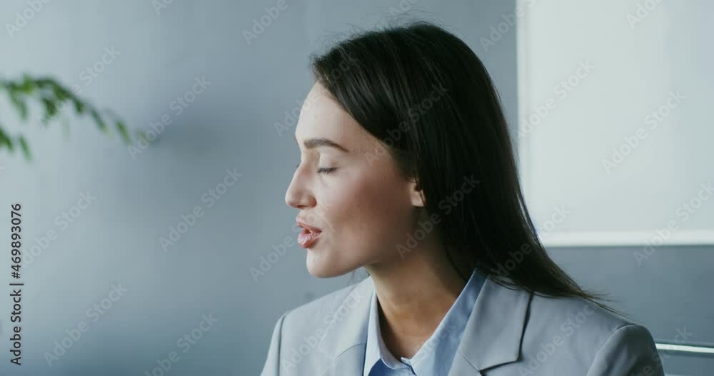 Young woman talking looking to the side, sitting at a table in a modern office Young woman talking looking to the side, sitting at a table in a modern office
