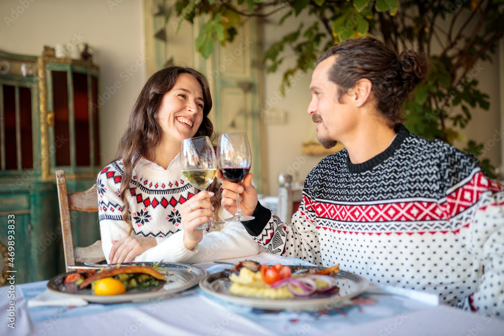 Smiling and happy multi-ethnic couple enjoying Christmas dinner in a rustic restaurant, making a toast Smiling and happy multi-ethnic couple enjoying Christmas dinner in a rustic restaurant, making a toast