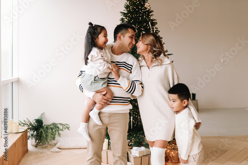 A happy diverse Asian family celebrates Christmas. Parents with children give gift boxes decorate the Christmas tree and prepare for the New Year holiday in a decorated house. Selective focus