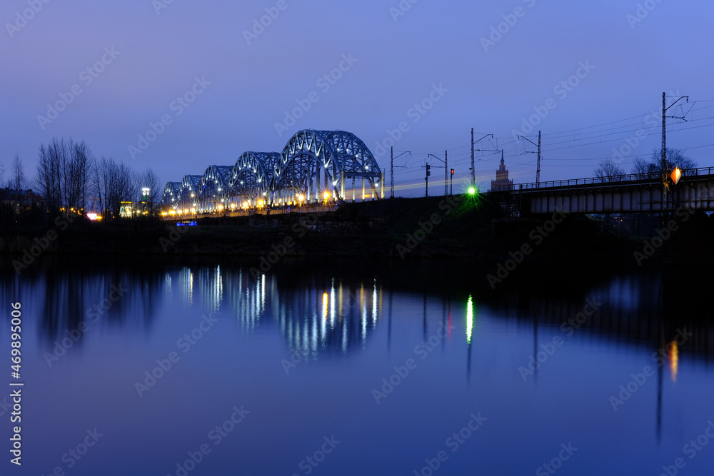 Reflection of night lights at dawn on the Daugava in Riga against the background of the railway bridge