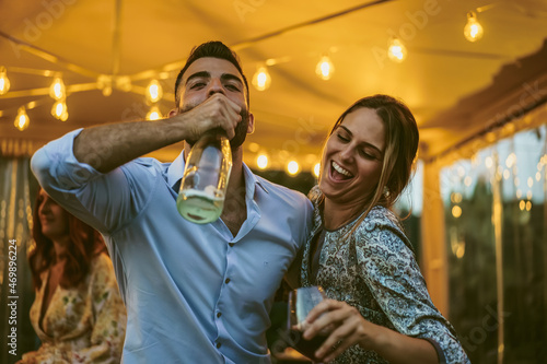 Couple of young friends having fun drinking at a party - drunk people dancing together
