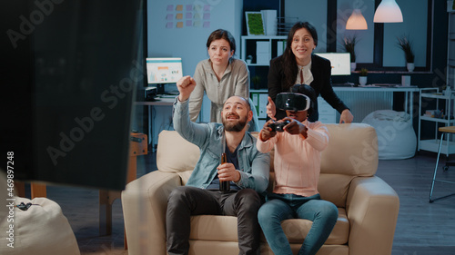 African american woman using vr glasses and controller to play video games while colleagues cheering for entertainment after work. Coworkers playing with technology to do fun activity
