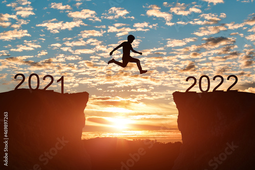 Happy new year 2022 concept. Silhouette of man jump on the cliff between 2021 to 2022 years over sunset or sunrise background.