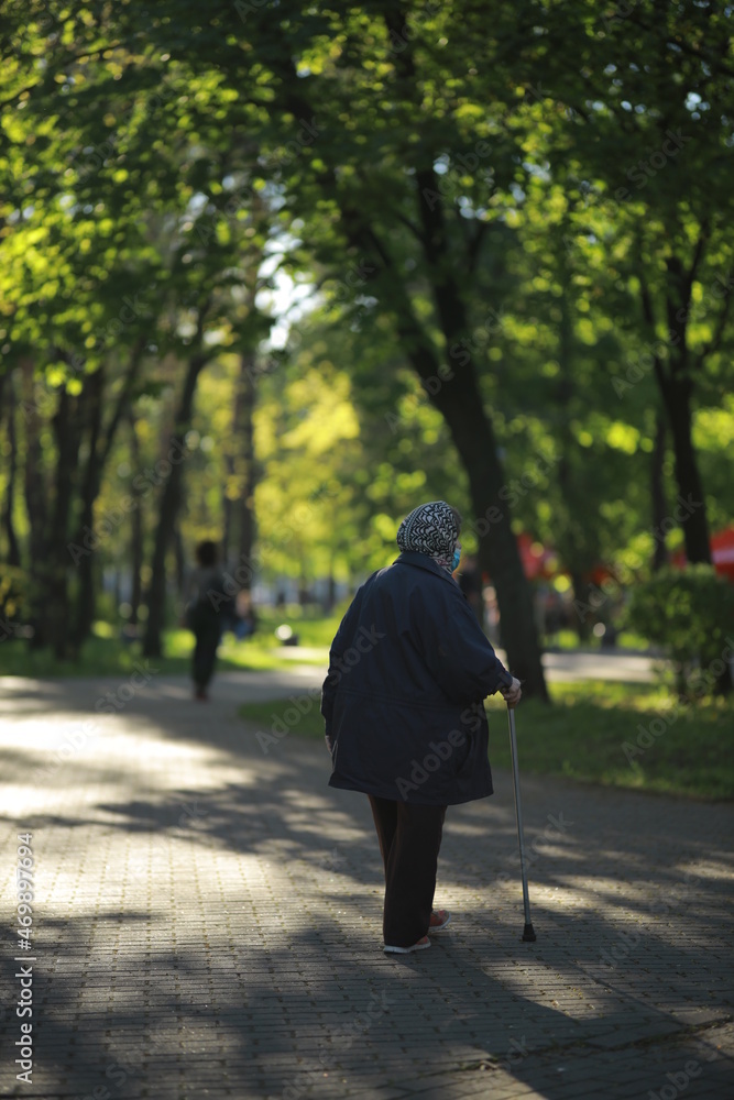 Grandmother walks in the park with a cane in a medical mask. Grandmother walks in the park with a cane in a medical mask.