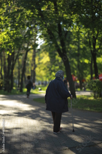 Grandmother walks in the park with a cane in a medical mask.