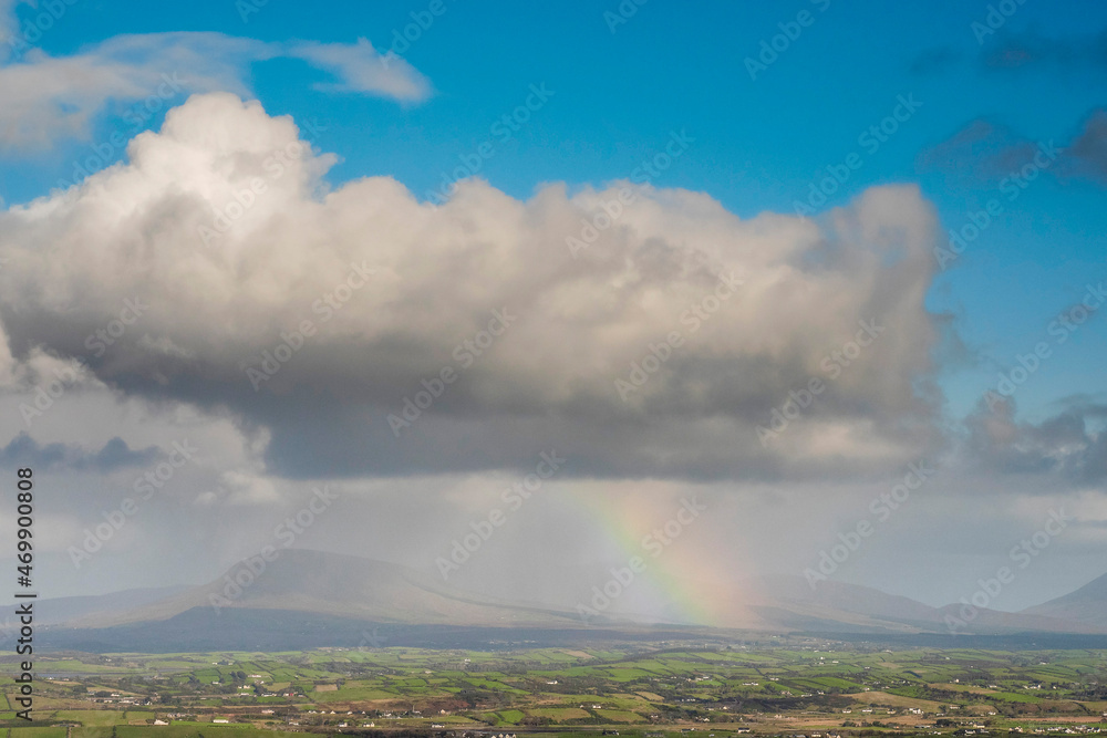 Rainbow under big cloud over green fields, mountains in the background. County Mayo, Ireland. Stunning nature scene.