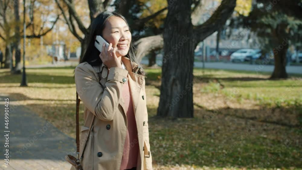 Slow motion portrait of Asian business lady walking in city street chatting on cellphone in autumn. Professional communication and urban lifestyle concept. Slow motion portrait of Asian business lady walking in city street chatting on cellphone in autumn. Professional communication and urban lifestyle concept.